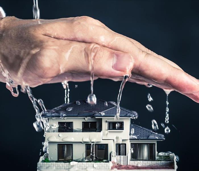 "Image of a wet hand dripping water over a small model home with a black background" 