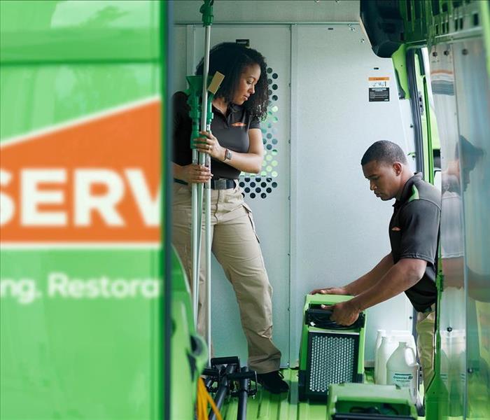 Image showing a first person perspective behind an open double door of a van, showing 2 Servpro technicians unloading the van