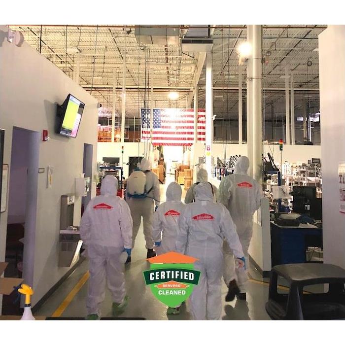 A crew of SERVPRO employees in PPE gear walking inside commercial building. 